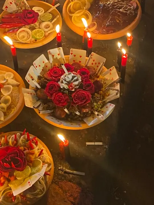 Alguidar de oferenda com rosas vermelhas e cartas de baralho, entre velas vermelhas acesas